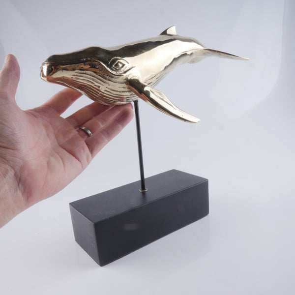 a hand holding a gold dolphin sculpture on a black stand